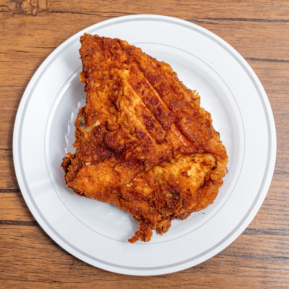Crispy fried chicken breast on a white plate with a gray rim, on a wooden table.