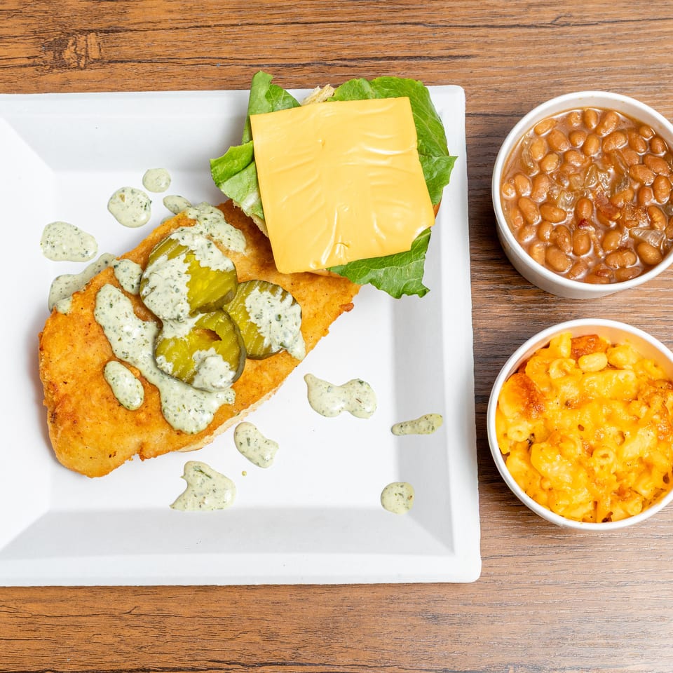 Fried chicken sandwich with lettuce, cheese, pickles, and creamy sauce served with baked beans and macaroni and cheese.
