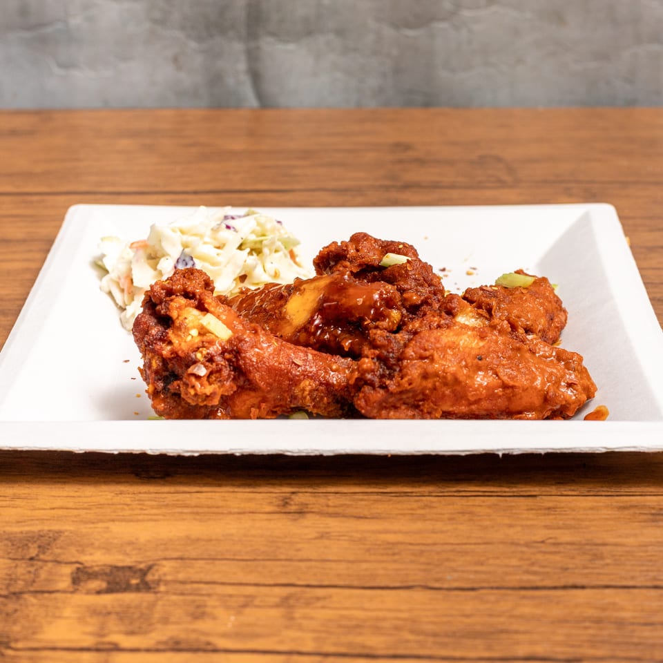 Spicy chicken wings with coleslaw on a white rectangular plate, on a wooden table.