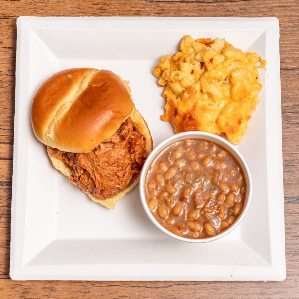 Pulled pork sandwich, baked beans, and mac and cheese on a white plate.