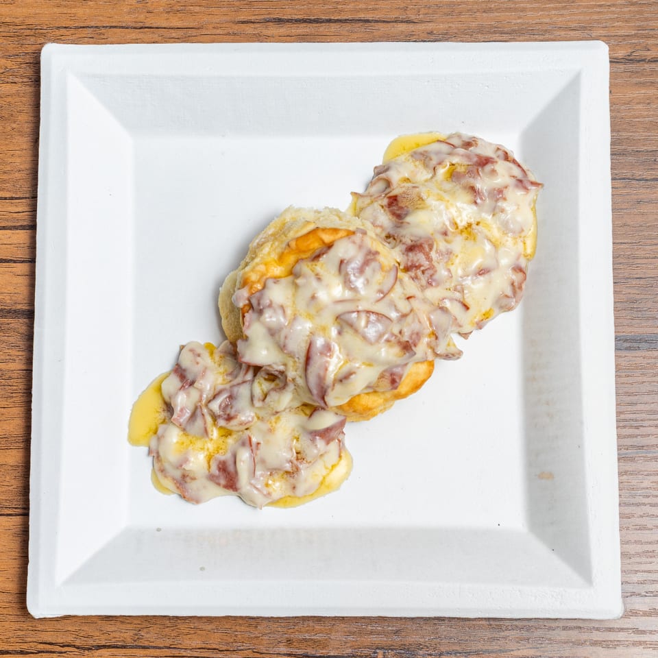 Two biscuits covered in creamy gravy with pieces of sausage, on a white rectangular plate.