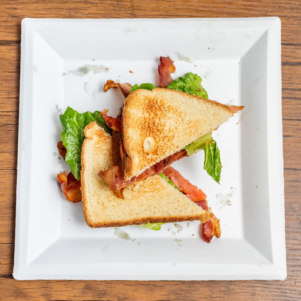 Overhead view of a BLT sandwich, cut in half, on a white square plate.