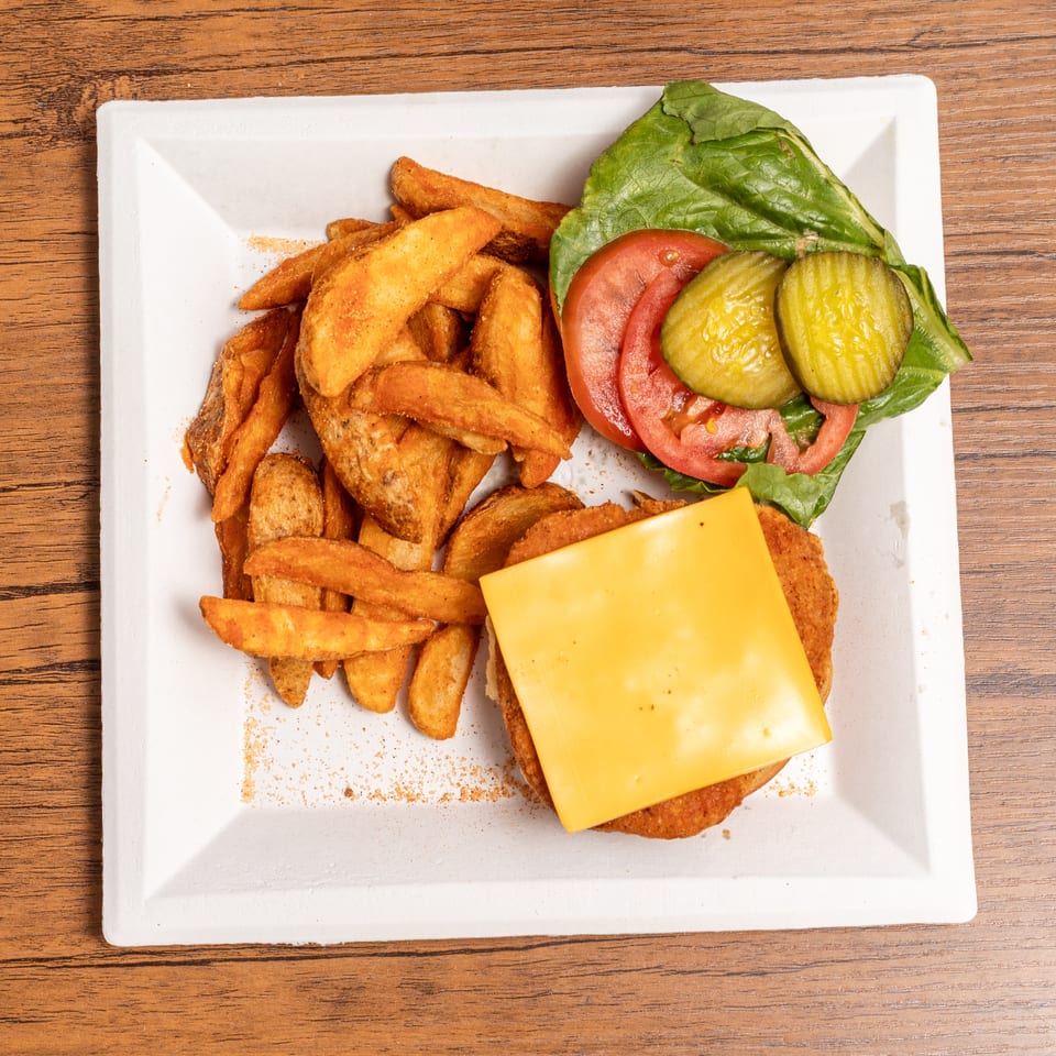 Chicken sandwich with cheese, lettuce, tomato, and pickles, served with seasoned potato wedges.